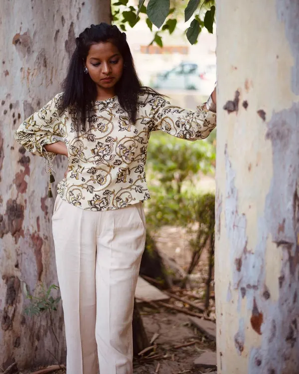 A full-length look at the Bagru print top paired with comfortable trousers. The natural setting and relaxed posture help customers envision themselves wearing this outfit for a casual day out. This is a key shot for a lifestyle clothing lookbook.