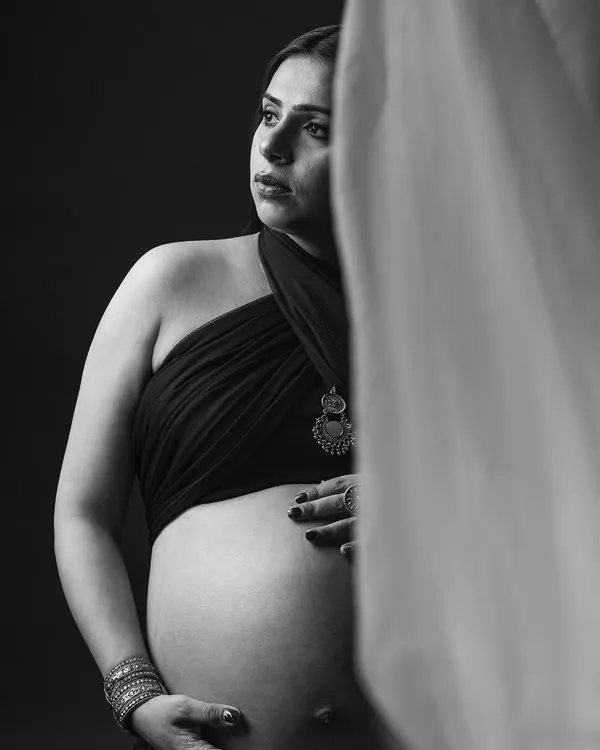 A quiet moment of reflection. This monochrome portrait uses soft light to highlight the beautiful curve of the baby bump and the mother's thoughtful expression.