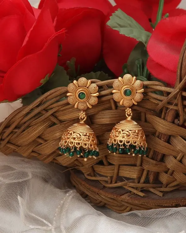 A lifestyle shot of traditional gold jhumkas with green beads, elegantly placed in a basket with red roses to create a rich, festive context for the jewellery.