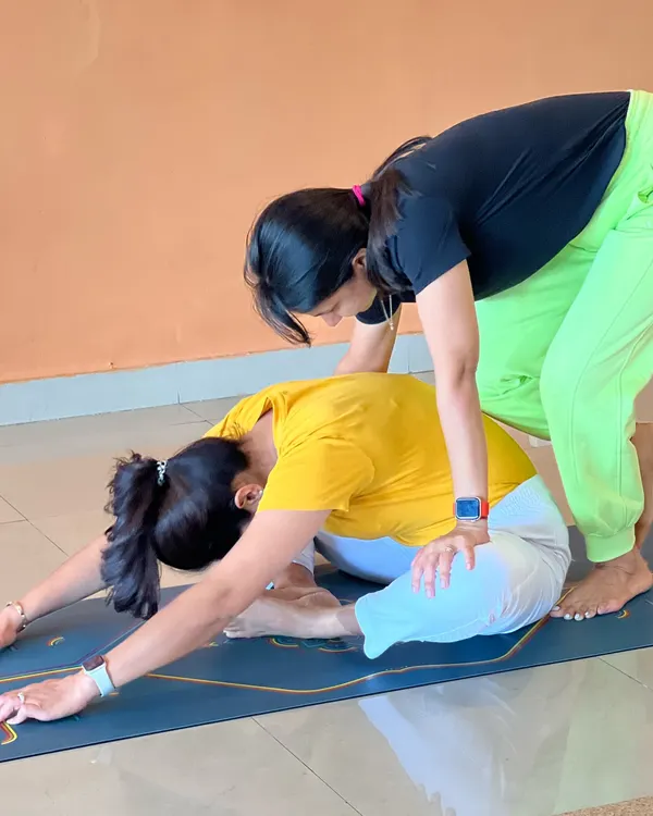 "Alone we can do so little, together we can do so much." A teacher assists a student in a forward bend, demonstrating the supportive nature of our community.