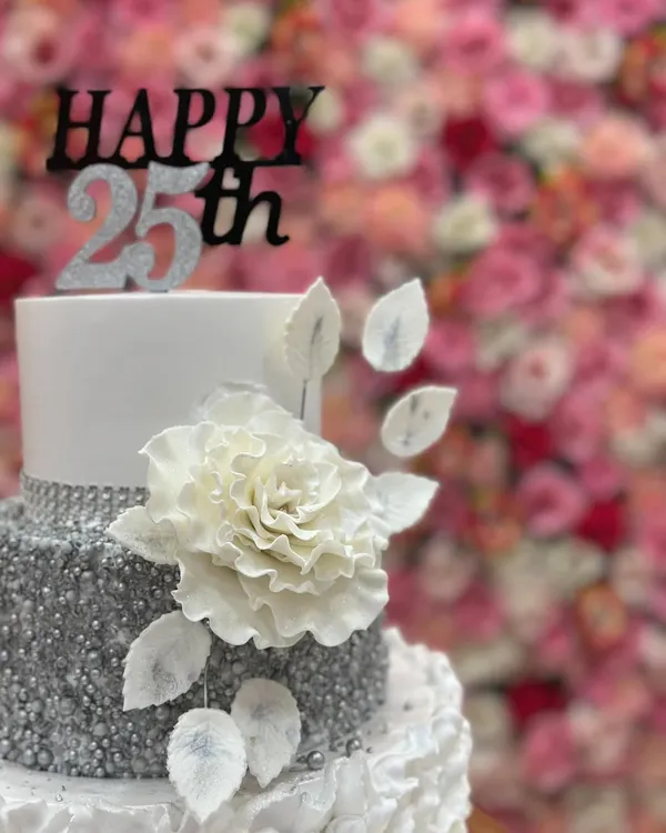 A close-up of the 25th-anniversary cake, focusing on the large, handcrafted white sugar flower and delicate silver leaves.