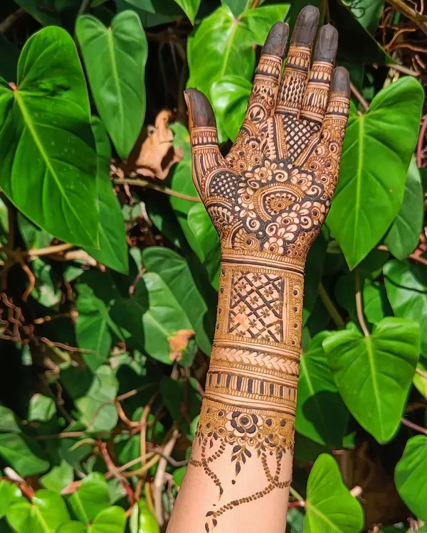 A beautiful design featuring a mix of geometric bands and a delicate vine pattern on the wrist, shot against a lush green background.