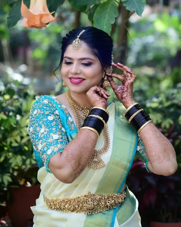 A candid moment of a bride getting ready. The focus is on her happy expression as she puts on her earrings, with her flawless makeup and hair already done.