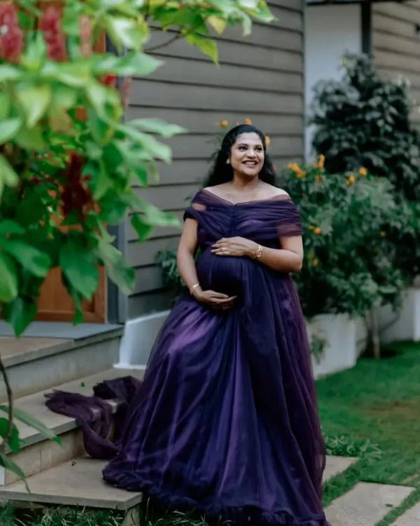 A happy client enjoying a quiet moment during her maternity shoot. The off-shoulder design and rich purple fabric of this rental gown are chosen for comfort and style.