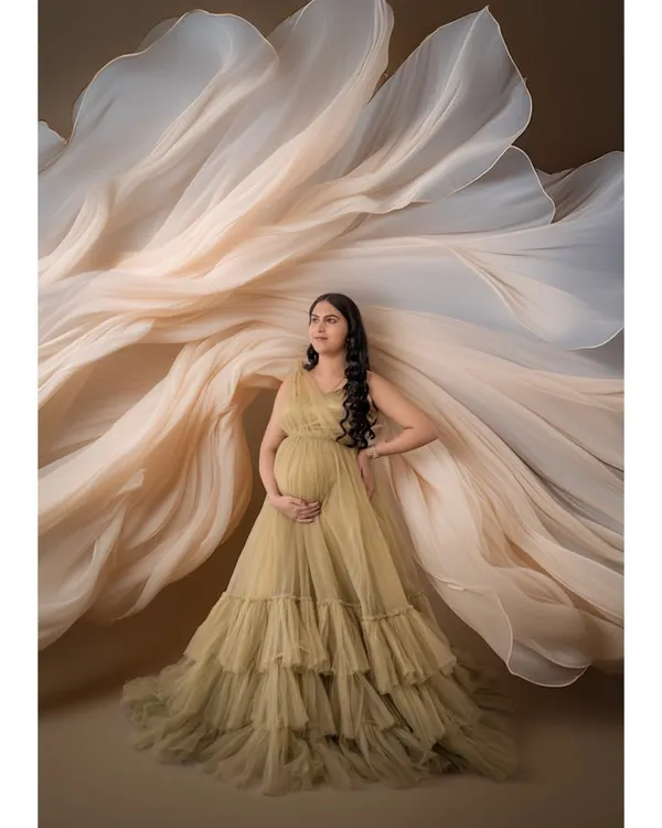 A dramatic shot featuring a mom-to-be in a golden-hued ruffled gown with fabric artfully arranged to create a fan-like effect. This showcases our creative styling options.