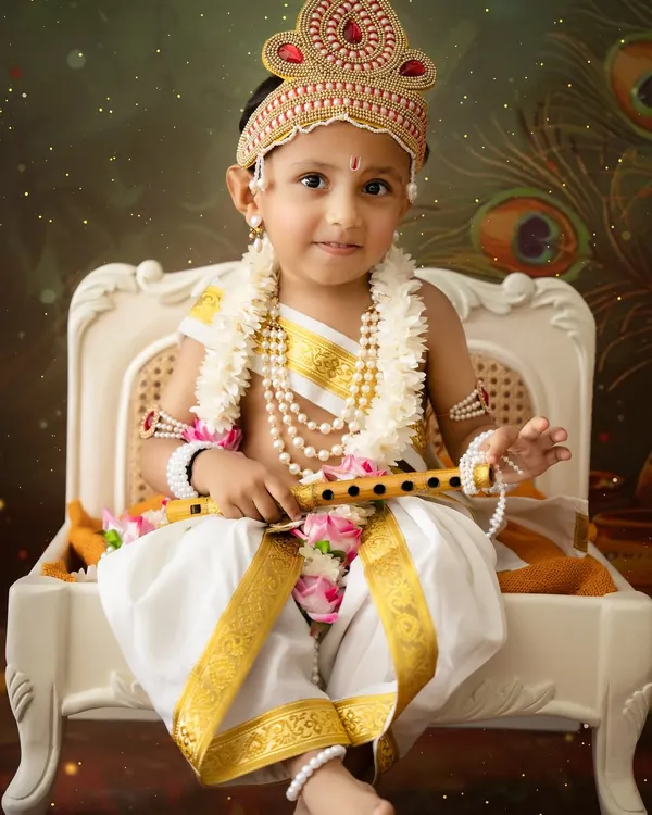 A stunning close-up of a young boy dressed as Lord Krishna, holding a flute. The detailed crown, pearl necklaces, and serene expression make this a powerful portrait.