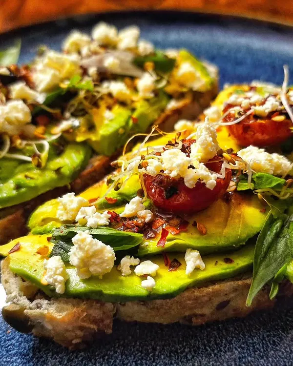 A delicious and healthy breakfast of homegrown avocado toast. It is topped with feta cheese, cherry tomatoes from the garden, and a sprinkle of chili flakes.