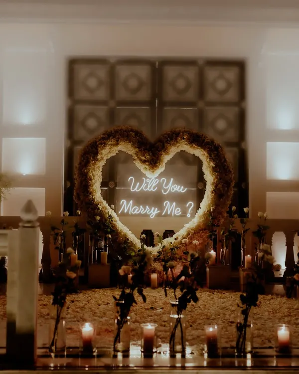 The perfect setup for a magical question. We capture all the beautiful details of your proposal decor, like this neon sign inside a heart of flowers, setting the stage for a resounding "Yes!".