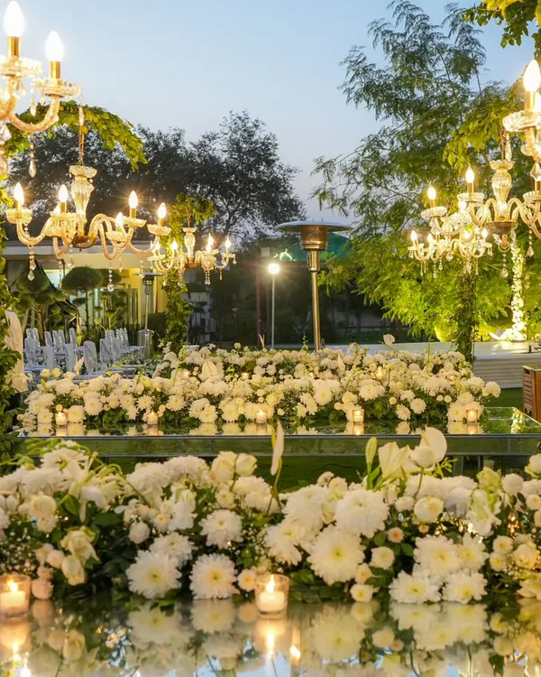 A breathtaking scene from a 25th-anniversary dinner. Mirrored tables are covered in a sea of white chrysanthemums and candles, reflecting the warm glow of crystal chandeliers above.