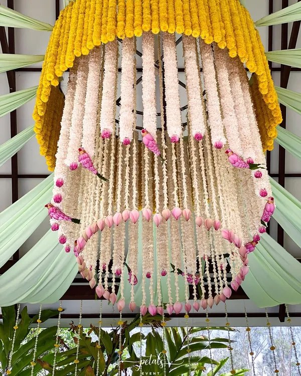 A magnificent floral chandelier, crafted from marigolds, tuberoses, lotus buds, and whimsical pink birds. This is a true statement piece, adding a touch of magic to the wedding decor.