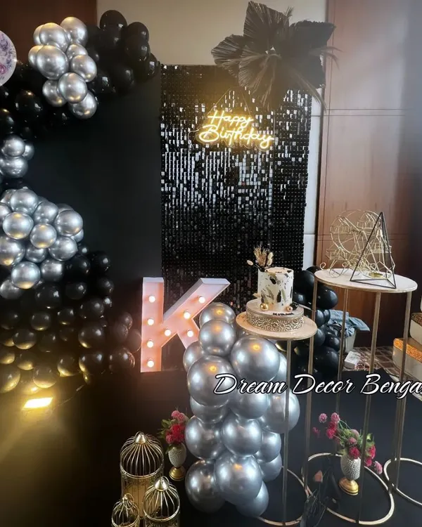 A sleek and stylish birthday setup in black and silver. The black sequin wall, 'Happy Birthday' neon sign, and metallic balloons create a glamorous and modern look.