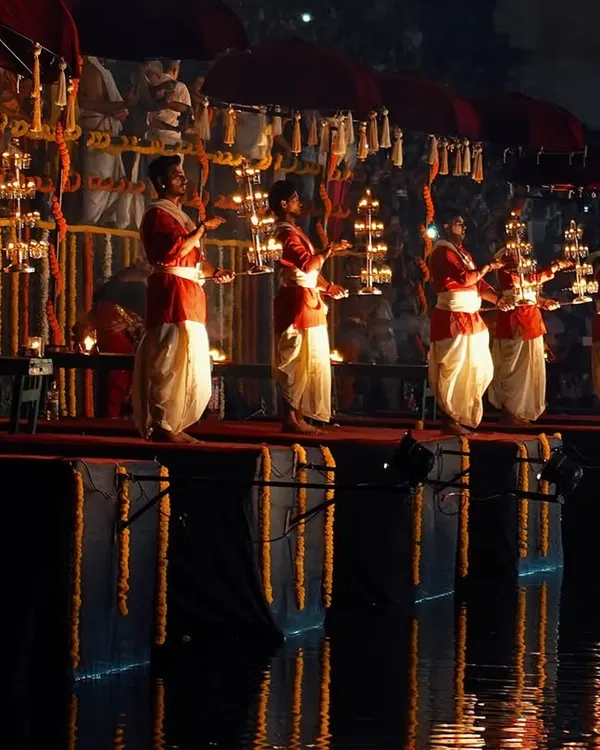 The serene Dev Deepawali Maha Aarti at Banganga Tank, with priests holding tiered lamps. The reflection in the water creates a truly magical, symmetrical scene.
