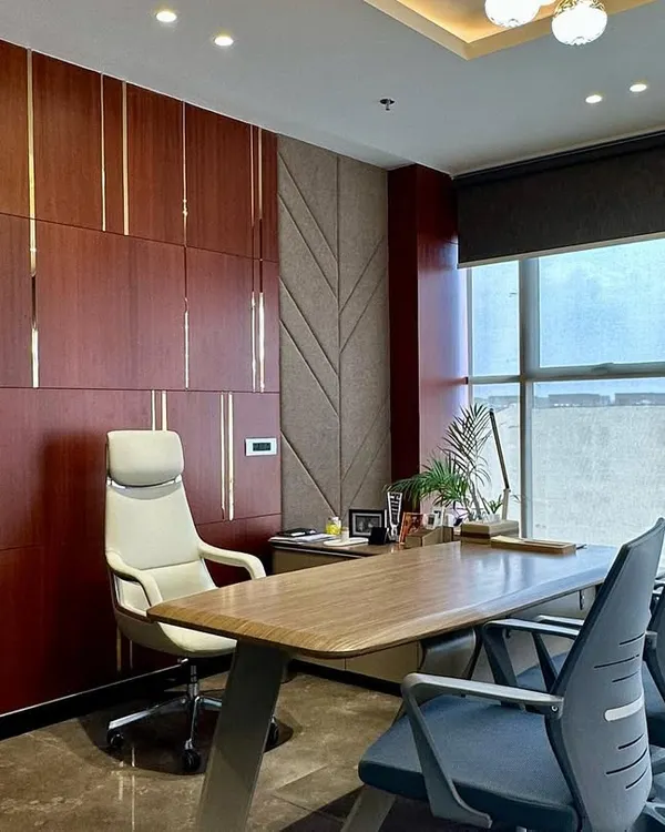 This MD room combines rich mahogany-toned wood panels with textured fabric sections and fine metallic strips. The ergonomic executive chair and spacious desk are positioned to take advantage of the natural light from the large window.
