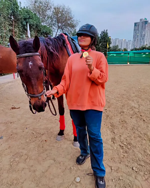 Celebrating a milestone! A student proudly shows off her medal after achieving a perfect canter, posing next to her trusted horse.