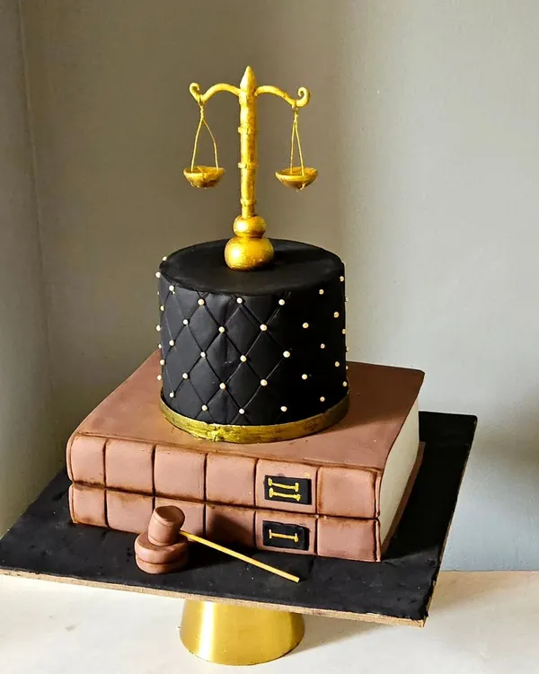 A cake for a lawyer, this design is both professional and artistic. It features two fondant-covered tiers designed to look like law books, topped with a quilted tier, an edible gavel, and the scales of justice.