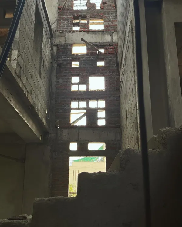 The central courtyard of a house under construction in Bangalore, viewed from the ground level. This image reveals the raw brick and concrete structure, with carefully planned openings that will soon flood the space with light.