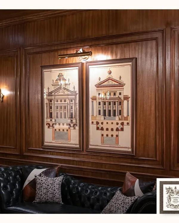 In this wood-paneled study, a classic picture light casts a warm, even glow over architectural prints, while a vintage-style wall sconce adds ambient light. This combination creates a sophisticated, layered lighting scheme.