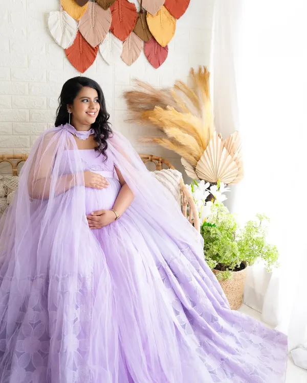 A radiant solo portrait of a mom-to-be in a flowing lavender gown, seated in a boho-chic studio setup with pampas grass.