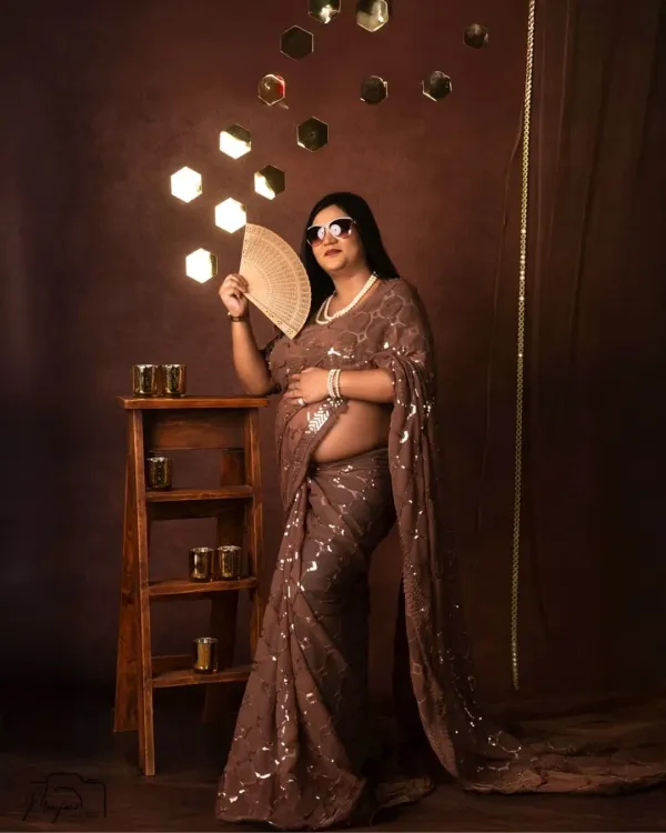 A glamorous and modern take on tradition. This mom-to-be shines in a sequined saree in our 'Shining Diva' setup, complete with stylish sunglasses and a fan.
