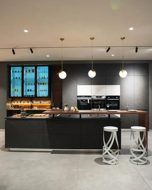 A stunning example of a dark and dramatic kitchen from our Coimbatore showroom. The combination of dark stone-finish cabinets, a wooden bar top, and back-lit glass units creates a luxurious, moody atmosphere perfect for entertaining.