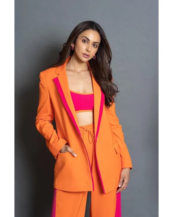 A full-length view of the vibrant orange and pink pantsuit from Antithesis. The wide-leg trousers and bold color blocking make it a modern power suit.