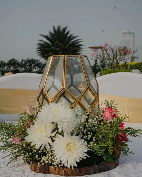 This centerpiece combines a modern gold-trimmed geometric lantern with a lush base of white chrysanthemums and pink roses. It's a perfect example of a small detail that adds a touch of warmth and sophistication to guest tables.