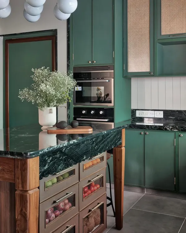 This kitchen is a study in rich, layered textures. The deep green of the cabinetry is balanced by the natural grain of the wooden island and the cool, veined marble countertop, creating a space that feels both grounded and full of character.
