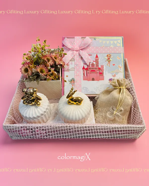 A delightful baby girl announcement hamper in a soft pink color palette. This gift set includes a themed box, decorative ceramic jars with golden animal motifs, and a small floral arrangement, all presented in a chic mesh tray.
