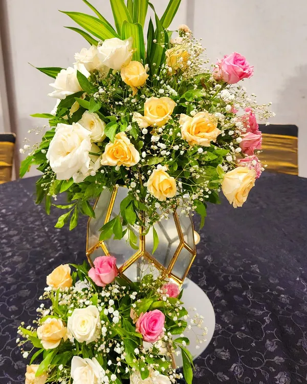 A close-up of a floral arrangement in a modern geometric vase, combining yellow, pink, and white roses for a fresh and elegant centerpiece.