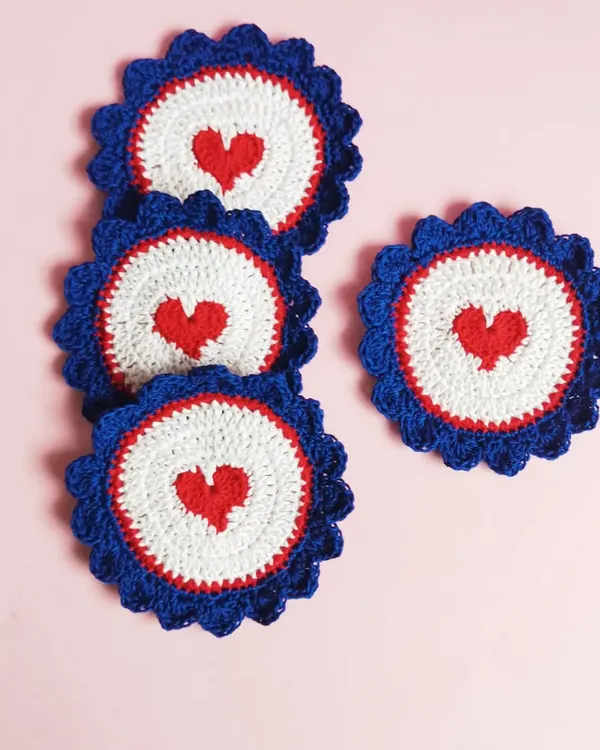 A set of our heart-themed crochet coasters. The design features a small red heart at the center of a white and blue scalloped circle, perfect for adding a little love to your coffee break.