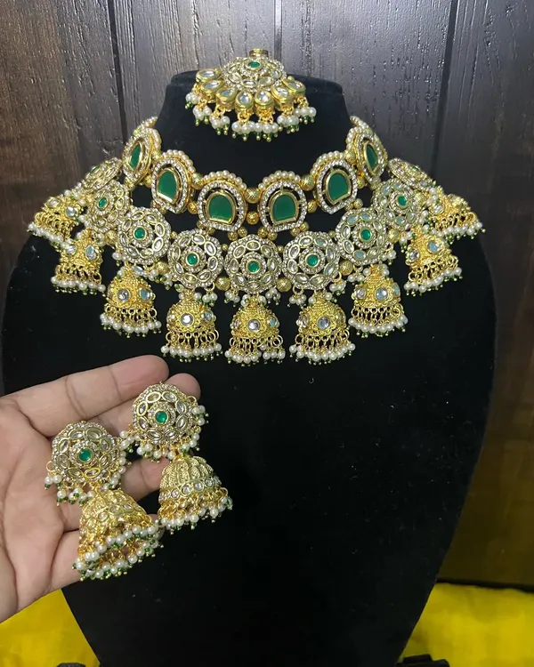 This stunning choker set is a favorite for sangeet or reception looks. It features intricate floral work with green stones and is adorned with multiple small jhumkas. The rental includes the choker, oversized matching jhumka earrings, and a maang tikka.