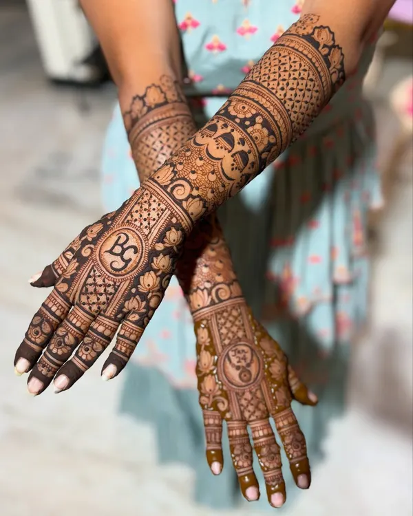 Gayathry's stunning wedding mehendi, featuring her and her partner's initials "BG" and a yin-yang symbol, surrounded by dense, traditional Indian patterns.
