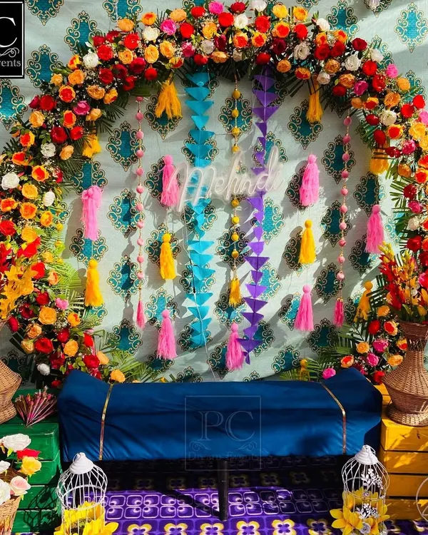 A riot of colors for a beautiful Mehndi ceremony. I designed this backdrop with a dense floral arch, a patterned teal wall, and colorful hanging tassels for a rich, layered look.