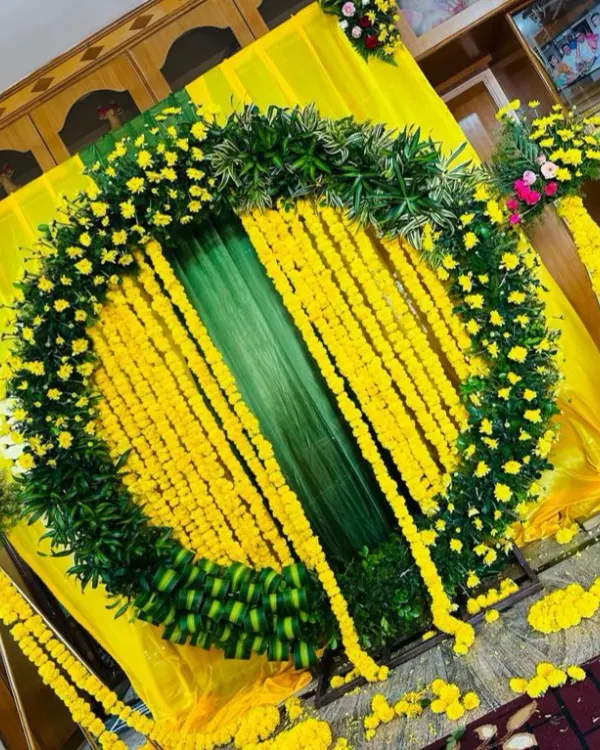 A classic Haldi ceremony decoration, featuring a large circular arch made of lush green leaves and bright yellow marigolds. The hanging flower strings add to the festive feel.