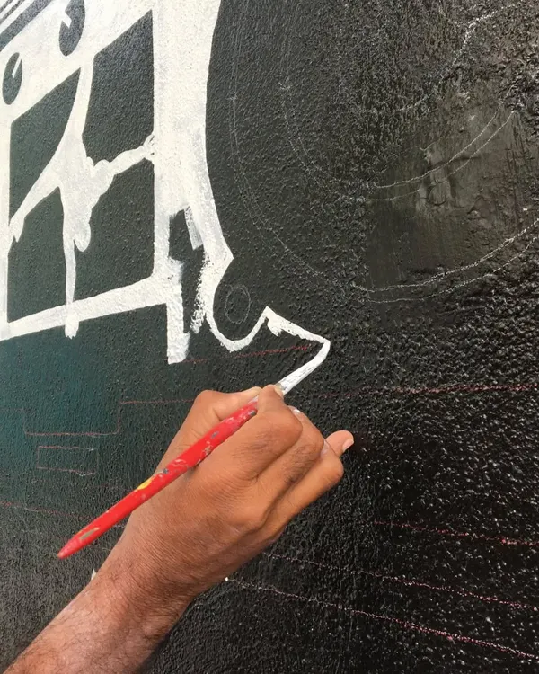 A close-up of our artist's hand, carefully painting a crisp white line on a black textured wall. This level of detail and control is what defines our custom mural work.