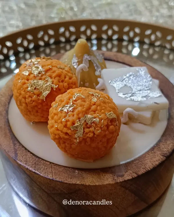 This wooden Indian dessert platter candle is a feast for the eyes. It features handcrafted wax versions of laddoos, a modak, and kaju katli, complete with gold and silver leaf details, all set in a beautiful wooden bowl.