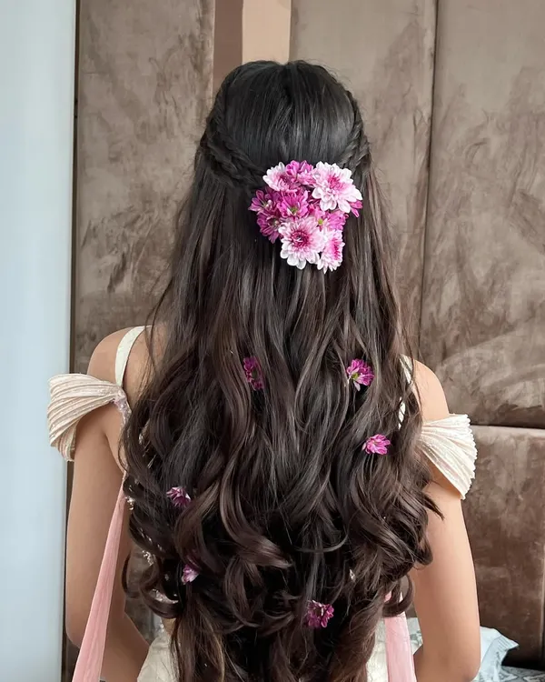 A beautiful half-up floral hairstyle perfect for a Mehendi or Haldi. The fresh pink daisies are woven through the hair for a soft, romantic look that complements the outfit.