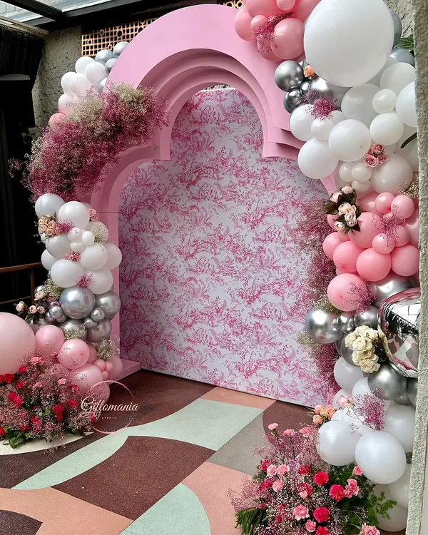 The main photo backdrop for a 40th birthday party with a Dior-inspired theme. The design features a custom-printed panel inside a pink arched structure, surrounded by a lush garland of pink, white, and silver balloons.