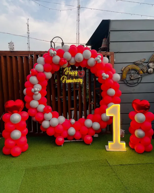 Celebrate your first year together with this vibrant outdoor setup. A circular balloon arch in red and silver frames a neon "Happy Anniversary" sign, with a large light-up number "1" making it a perfect photo opportunity.