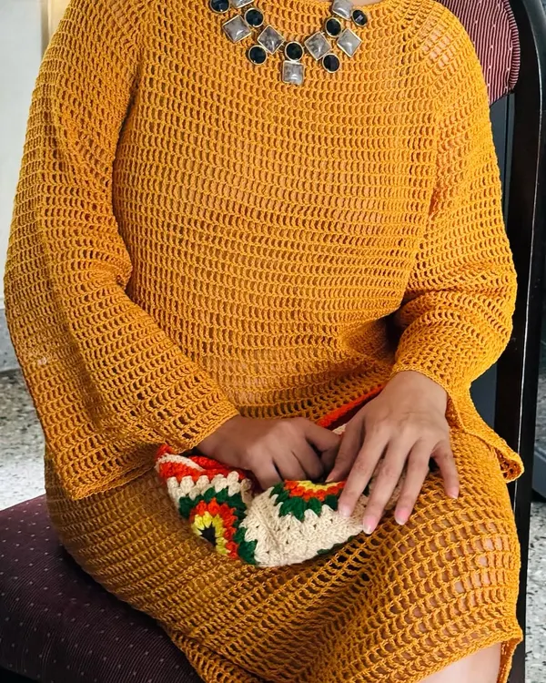 A closer look at the mustard crochet dress, showing the texture of the stitch work and how it drapes beautifully when seated.