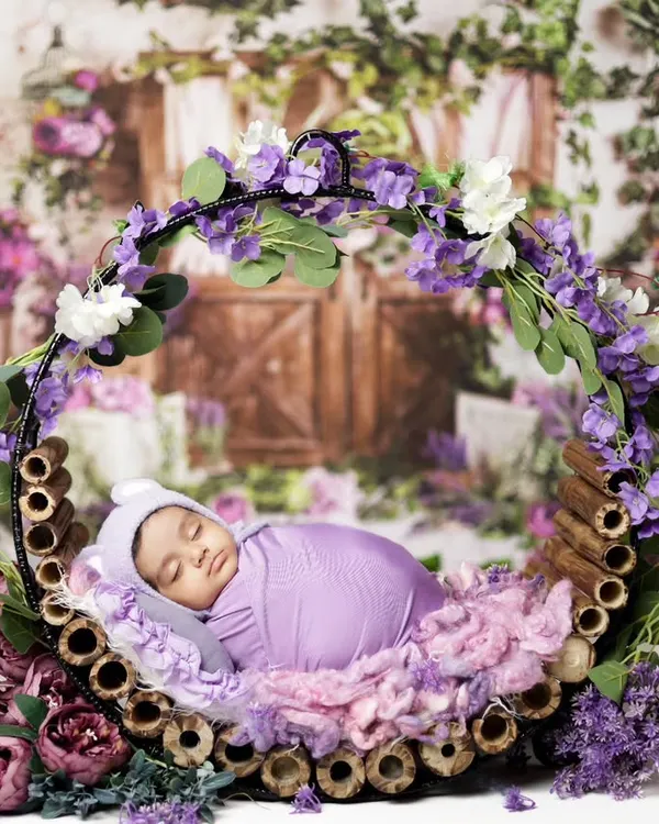 This peaceful newborn is resting in a floral hoop, surrounded by soft purple flowers. We designed this setup for an at-home session in Jaipur, bringing all the props to ensure the baby and mom are comfortable.
