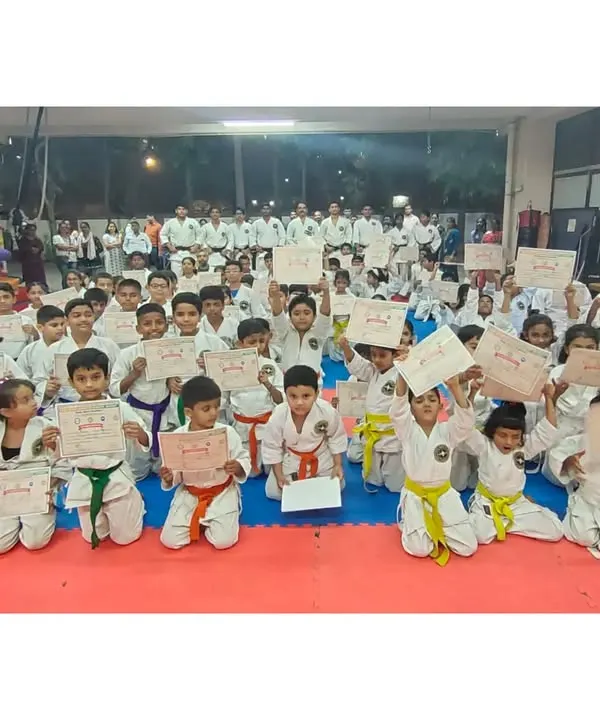 A hall full of smiling students holding their new certificates after a successful belt grading exam. This is a proud day for them and their parents.