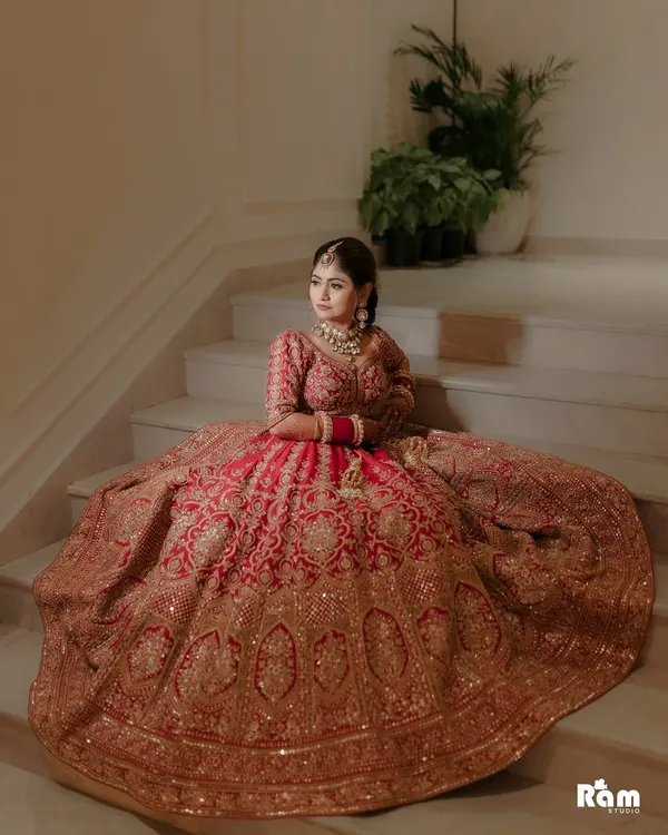 A breathtaking portrait of the bride seated on a grand staircase, her magnificent red and gold lehenga spread out around her. This shot is all about royal elegance and capturing the bride in her full splendor.