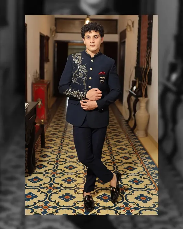 This navy blue Bandhgala suit is a perfect example of modern royalty. It features asymmetrical gold embroidery that flows from the shoulder down the chest, paired with a custom pocket crest. The entire look is tailored for a sharp, commanding presence.