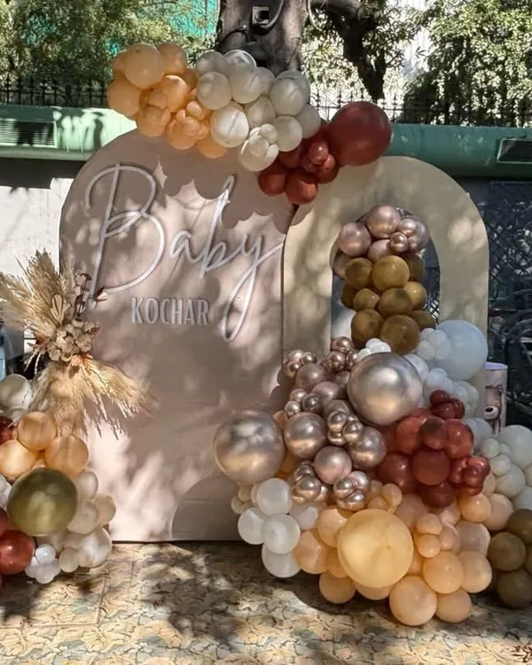 A chic boho-style baby shower backdrop with earthy-toned balloons, pampas grass, and a personalized "Baby Kochar" sign.