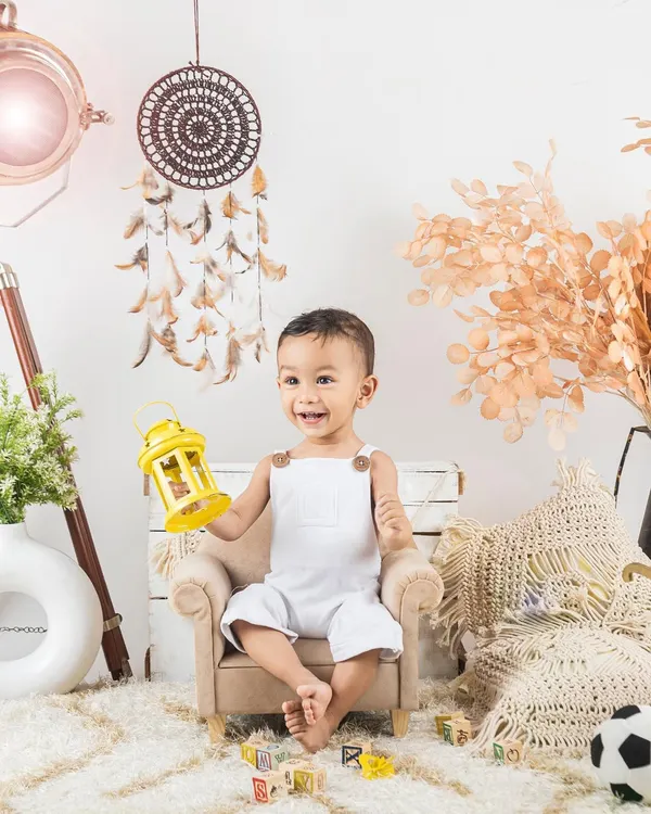 A happy little boy in a simple, bright white outfit, sitting in a mini armchair. This lifestyle setup with a dreamcatcher is one of my favorites.