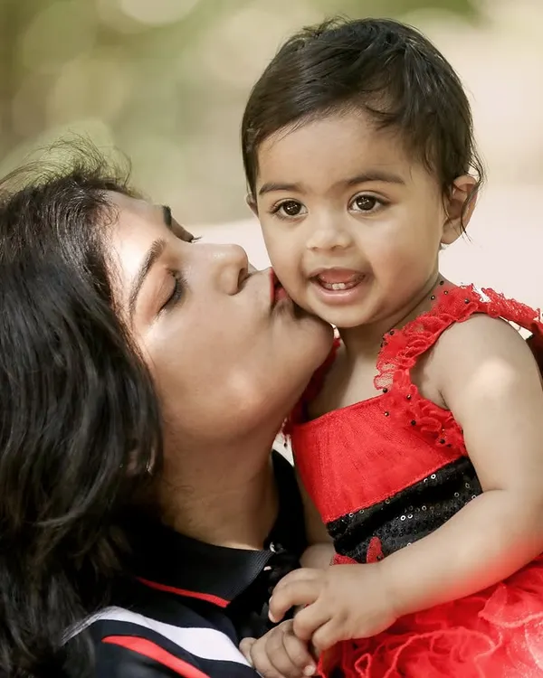The pure joy of a mother's kiss. This candid outdoor shot captures a beautiful, unposed moment of affection between a mother and her smiling baby.