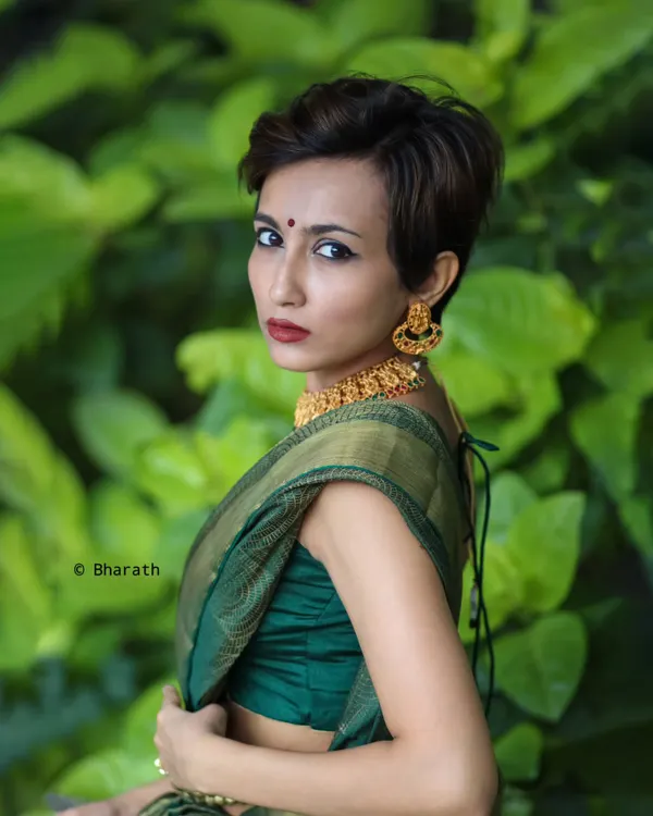 A bold and modern take on ethnic wear. This portrait features a model with a pixie cut wearing a traditional green silk saree, creating a striking contrast that challenges conventions.