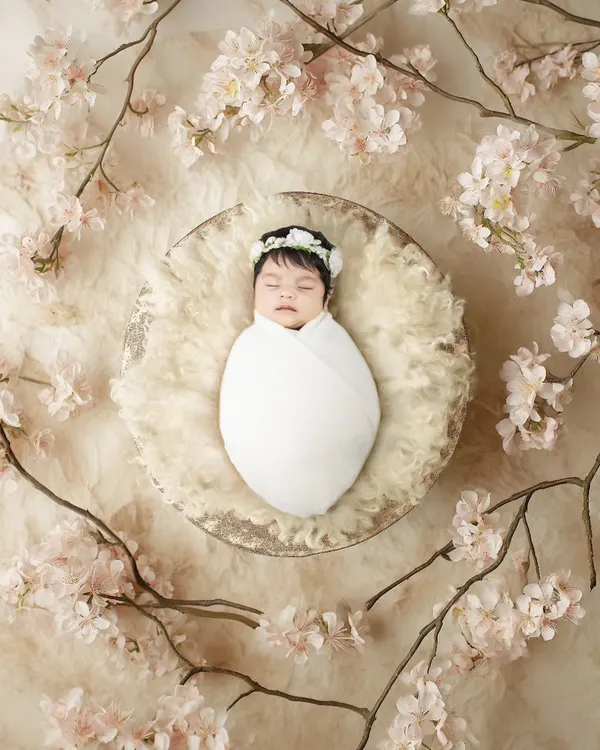 A newborn baby peacefully sleeping in a basket, surrounded by delicate cherry blossoms. This is such a serene and beautiful way to photograph the newest member of your family.