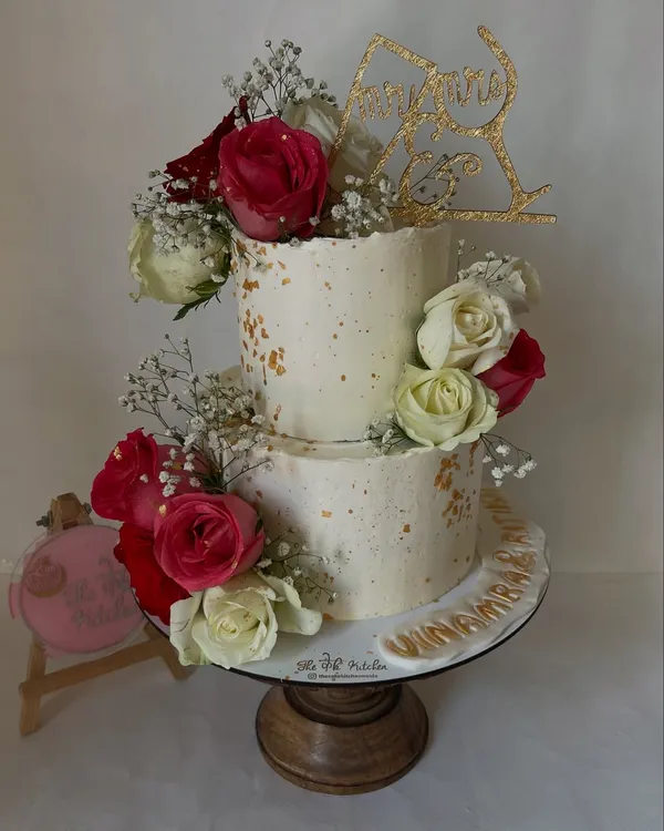 A rustic and romantic two-tiered wedding cake, featuring a textured buttercream finish, gold leaf specks, and an arrangement of fresh red and white roses.